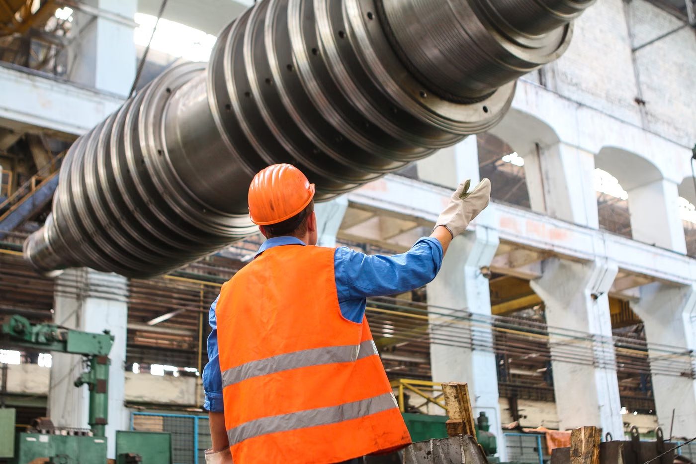 Worker guiding a craned turbine rotor inside an industrial plant